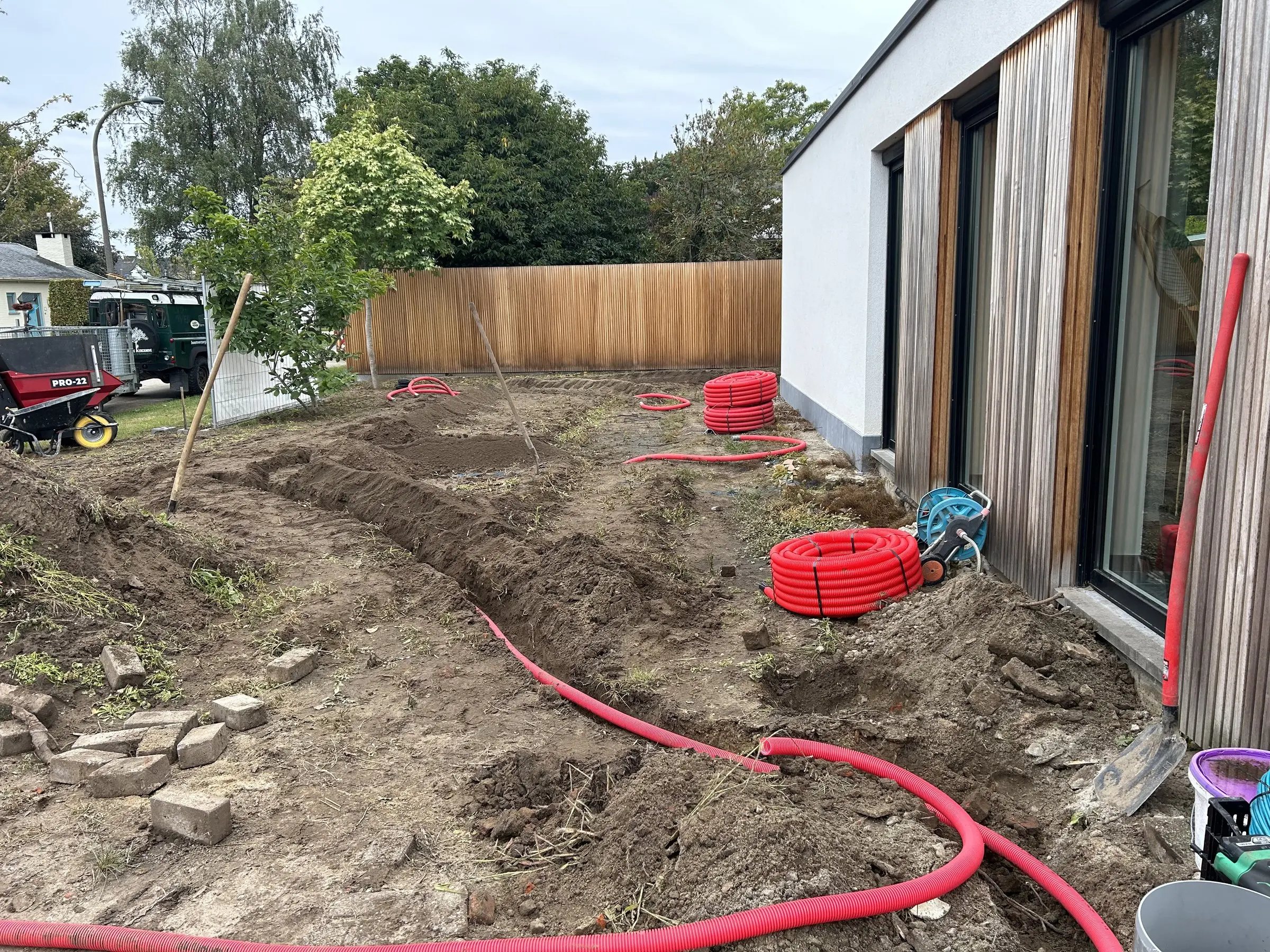Sleuf met rode kabelbuizen naast de woning