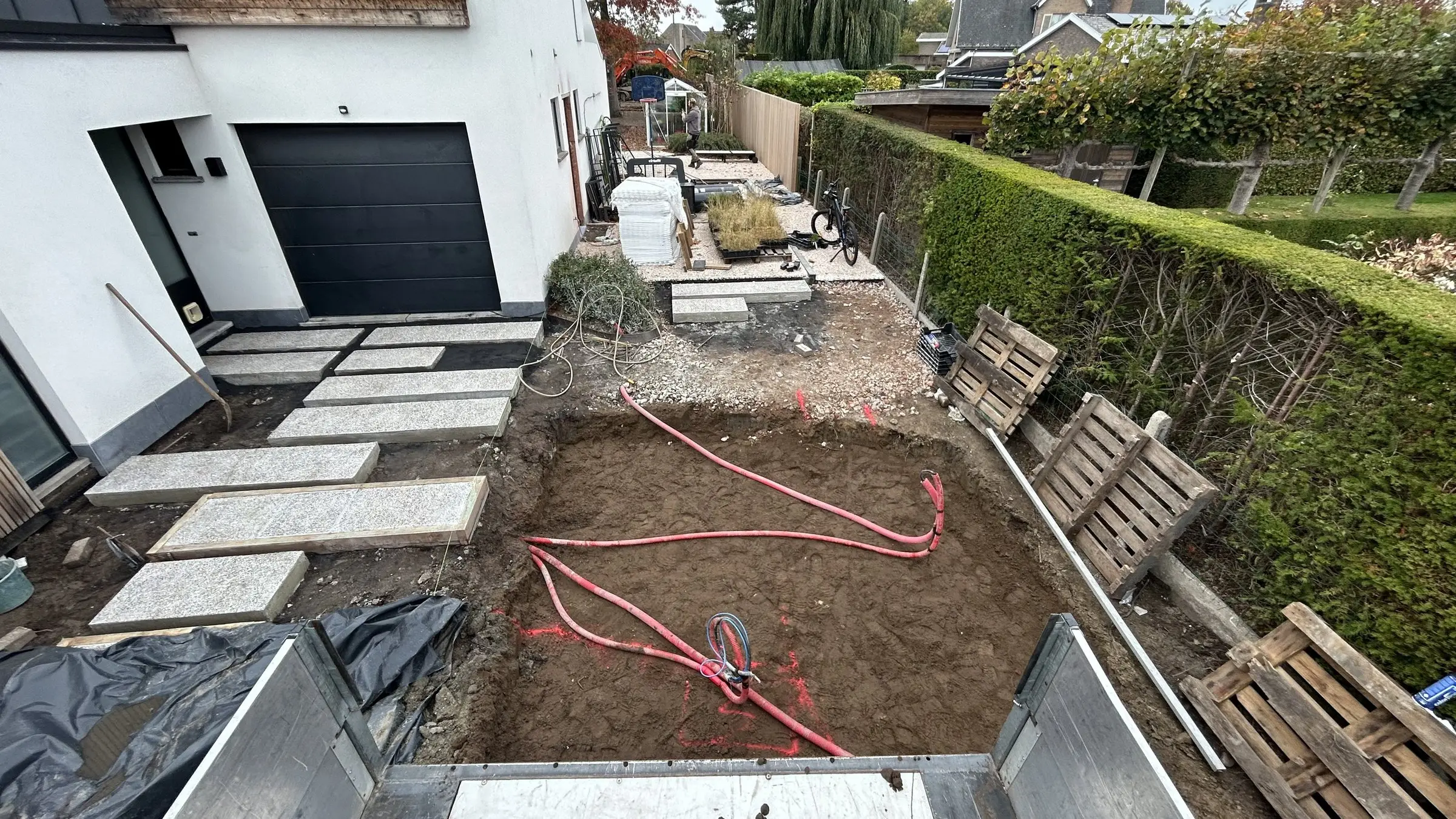 Uitgraving naast een oprit met stapstenen en leidingen