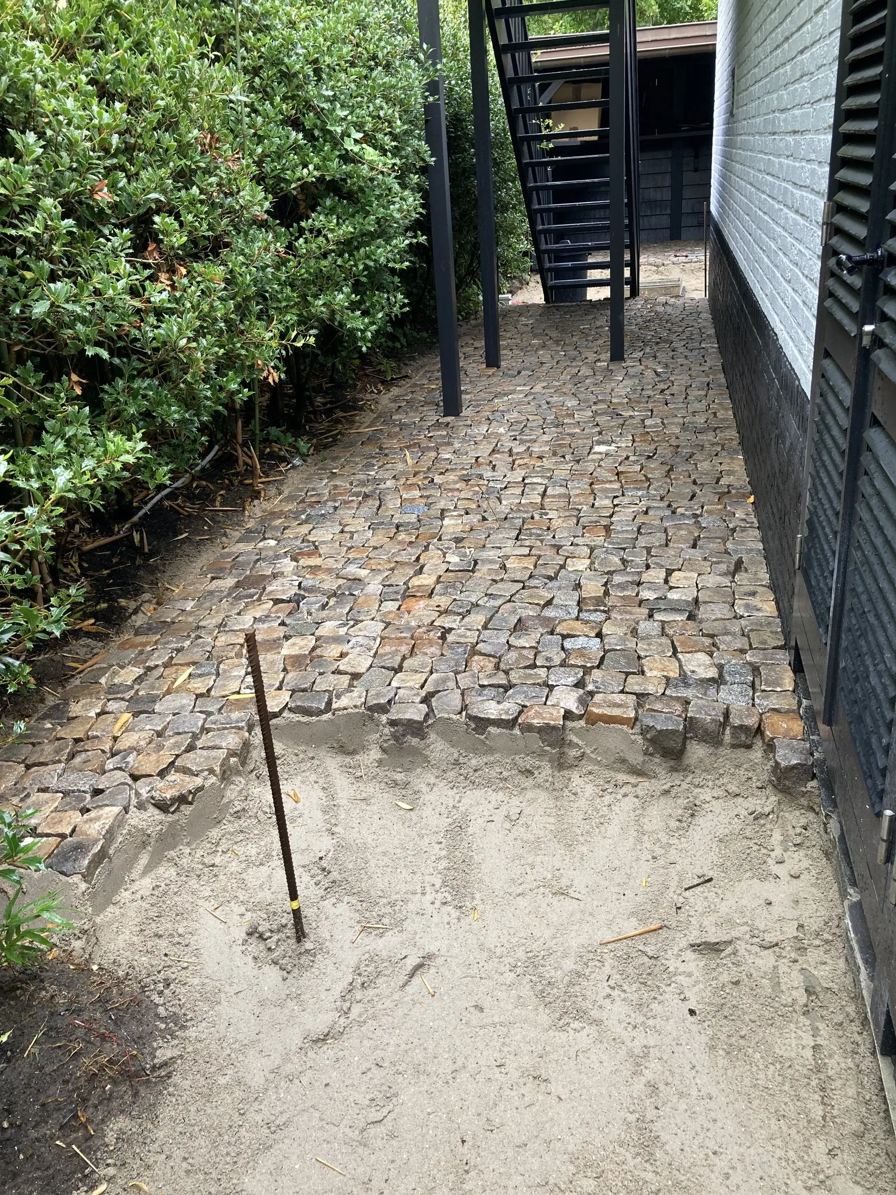 Smal pad langs de gevel, zandbed klaar voor de kasseien