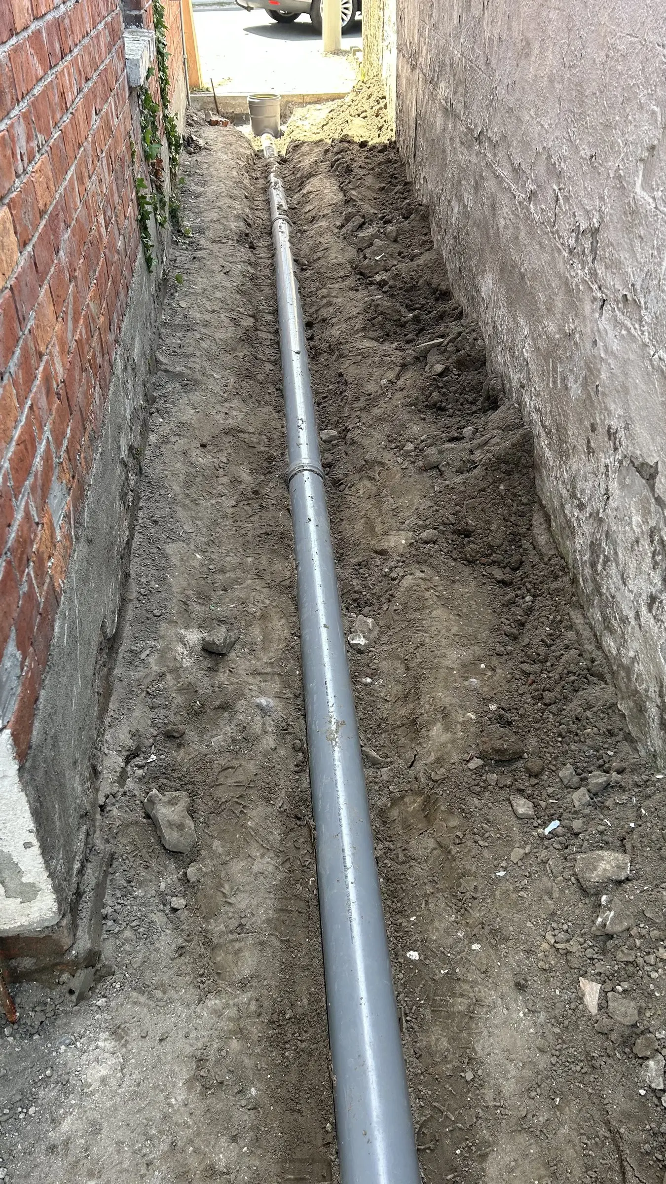 Lange nieuwe buis in de sleuf langs de muur