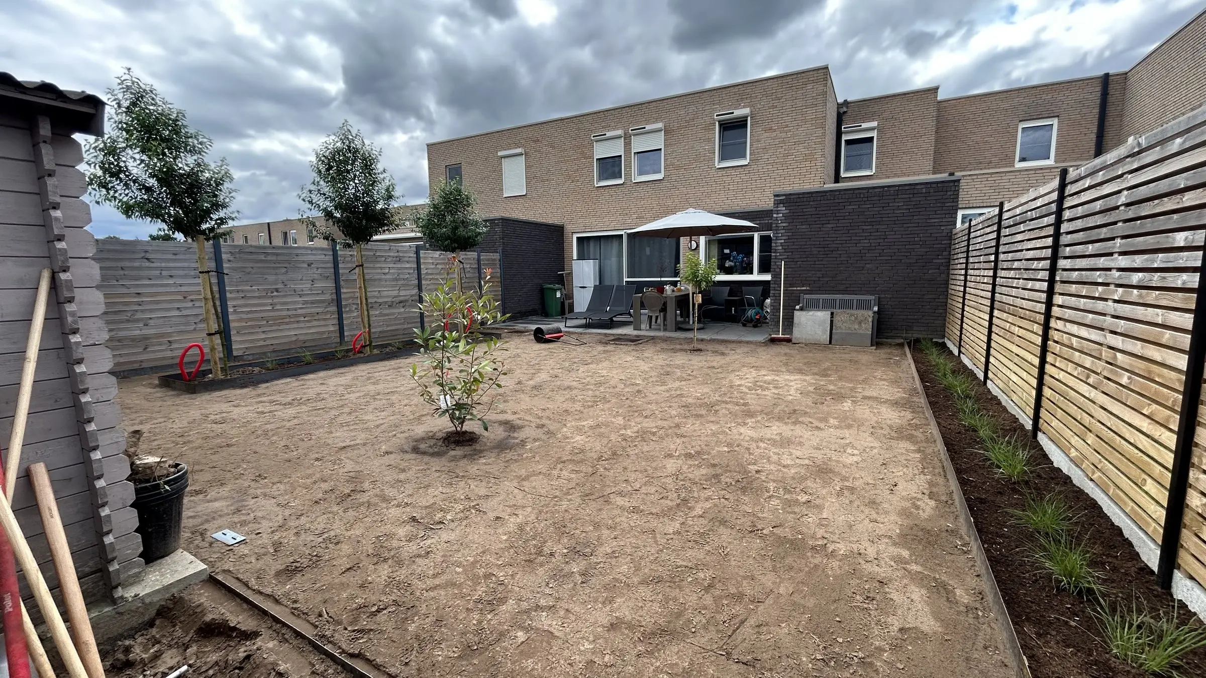Vlakke zandgrond met eerste beplanting en de tuinberging