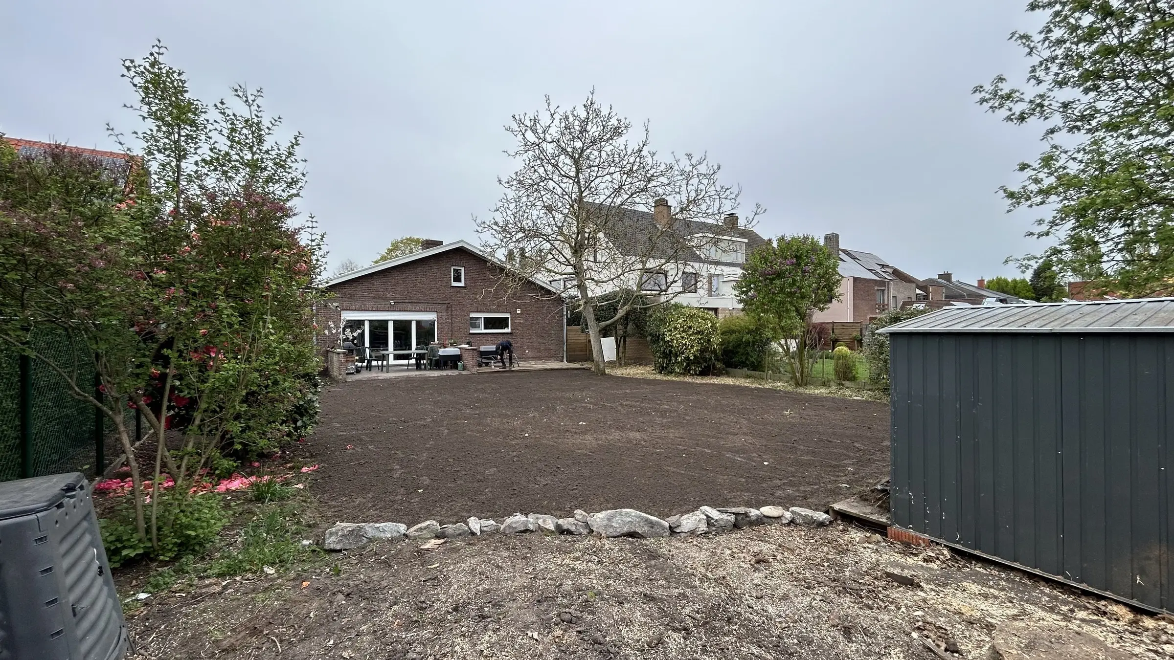 Vlakke, donkere grond met tuinberging op de achtergrond