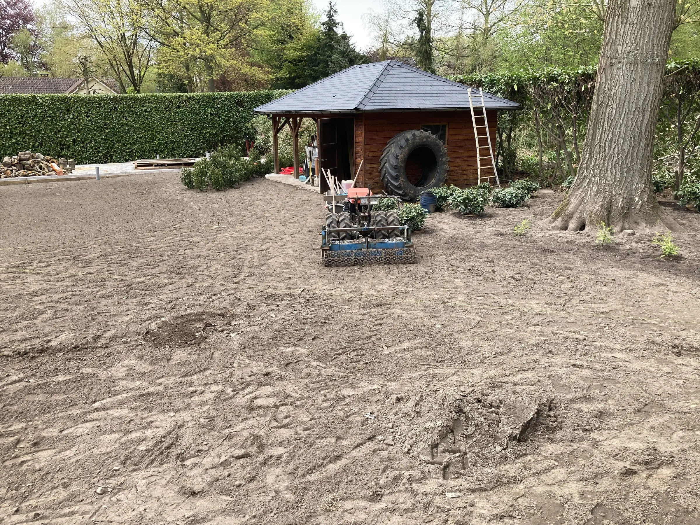 Open, vlak gemaakt terrein met het tuinhuis op de achtergrond