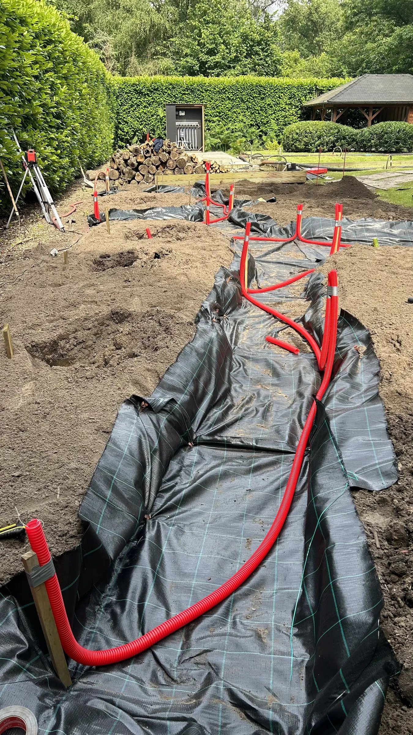 Leidingsleuf met folie en rode buizen in de tuin