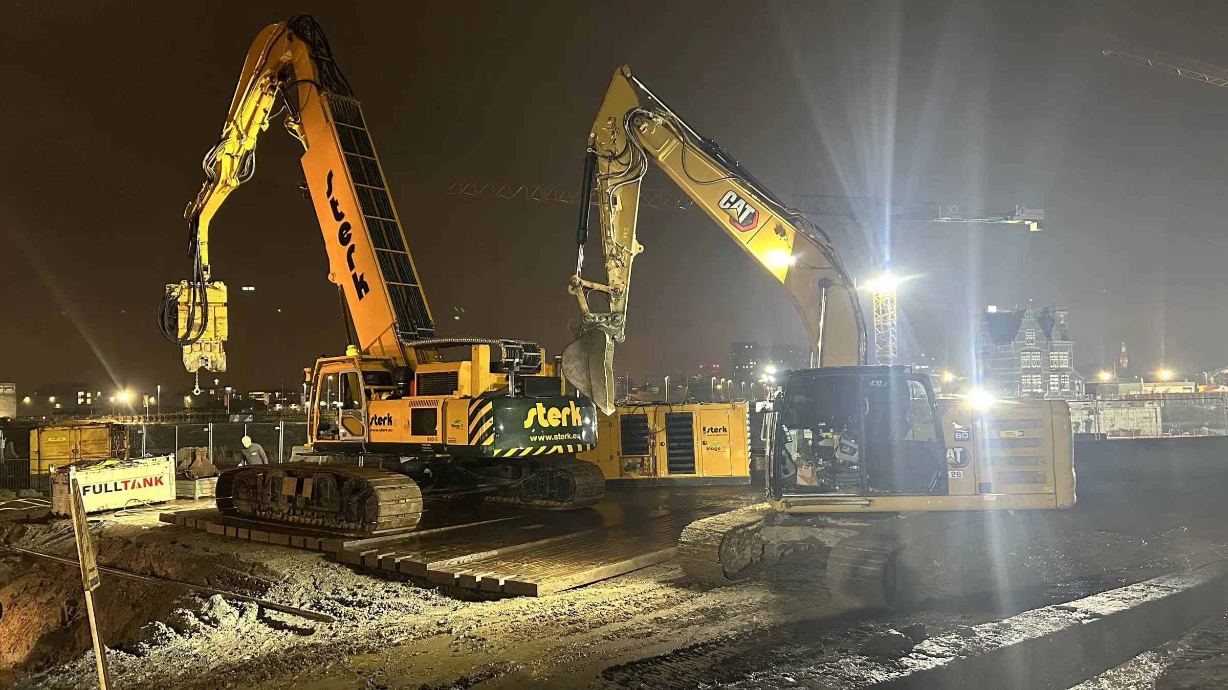 Twee gele sloopmachines bij avond op de werf