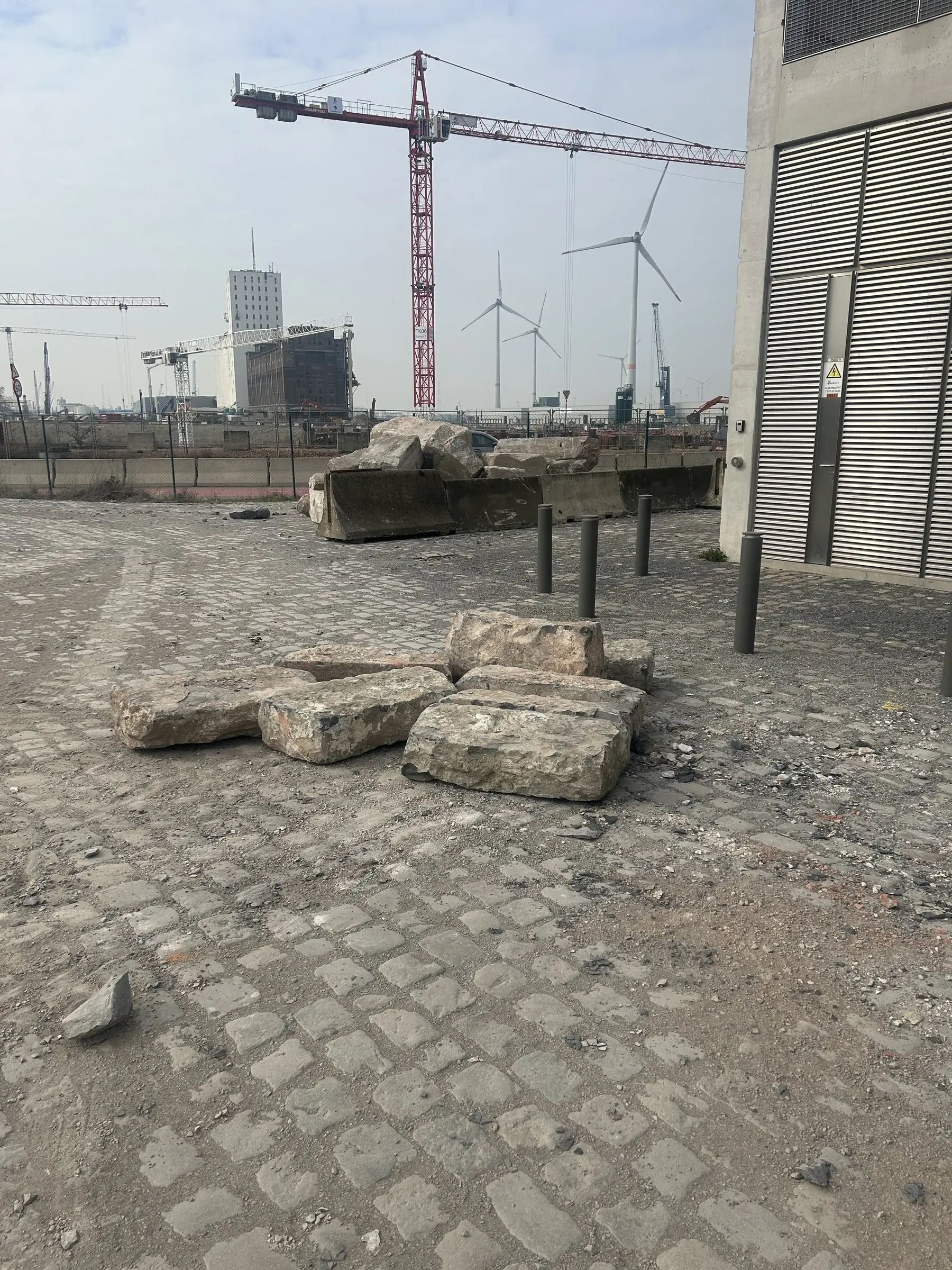 Vrijgemaakt terrein met kasseien en kranen op de achtergrond